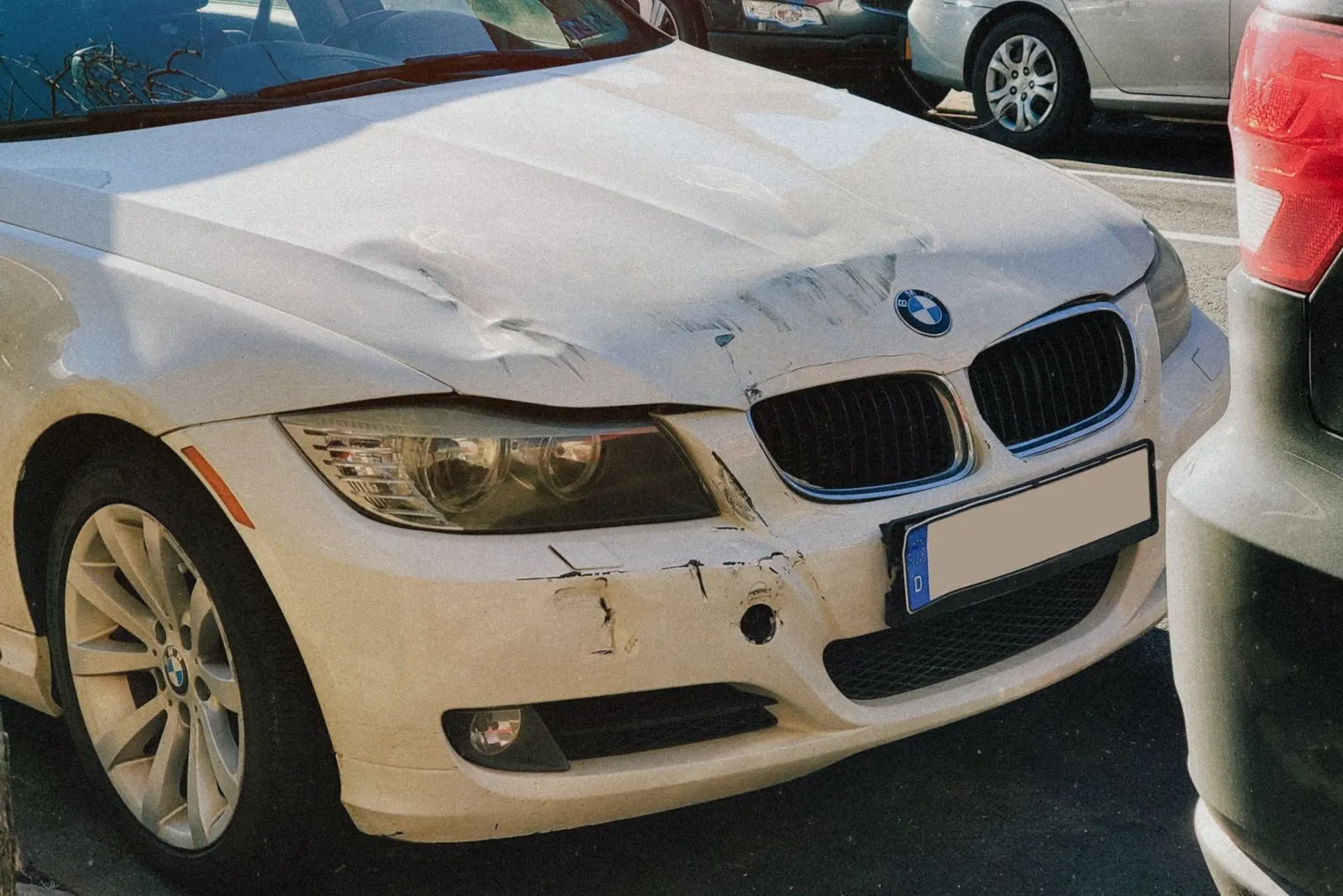 Coche blanco con el frontal abollado, parado en la calle después de un golpe