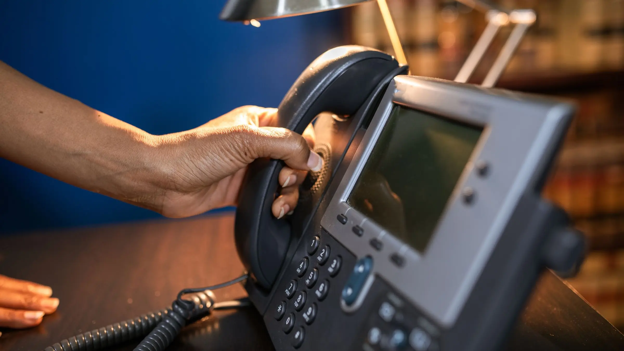 Mano descolgando el teléfono de sobremesa de un despacho